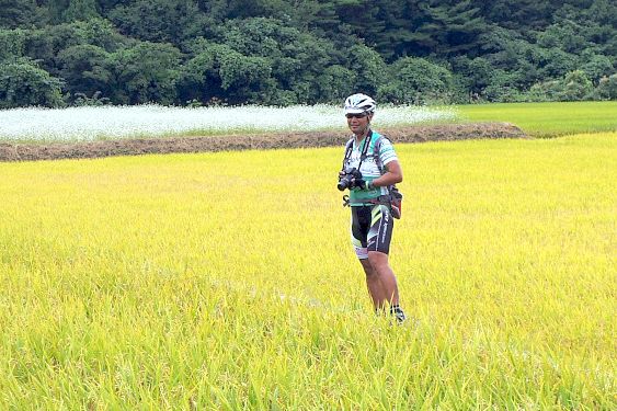 田んぼの中でひとりシャッターチャンスを覗う編集長。